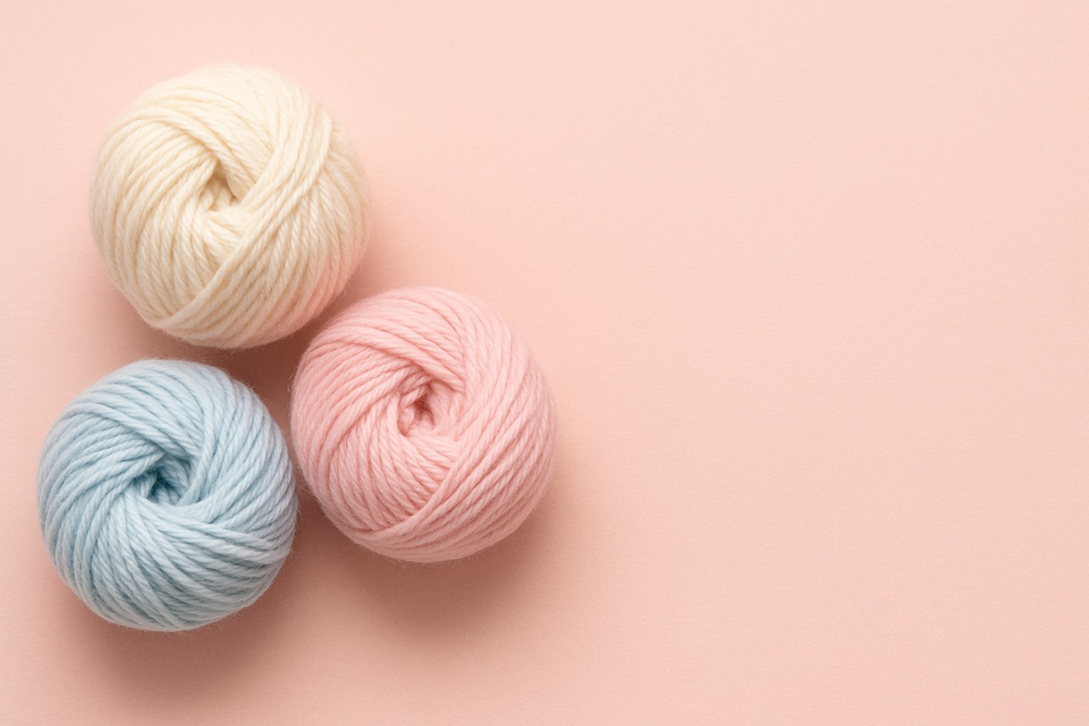 3 Gomitoli belli e ben raggomitolati di lana su sfondo rosso chiarissimo tutti sul lato sinistro e lato destro libero da niente