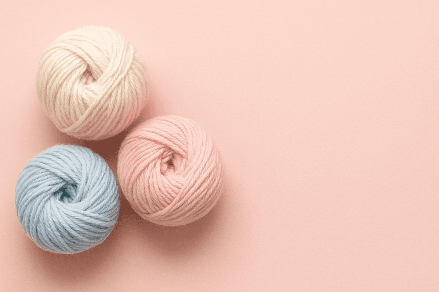 3 Gomitoli belli e ben raggomitolati di lana su sfondo rosso chiarissimo tutti sul lato sinistro e lato destro libero da niente